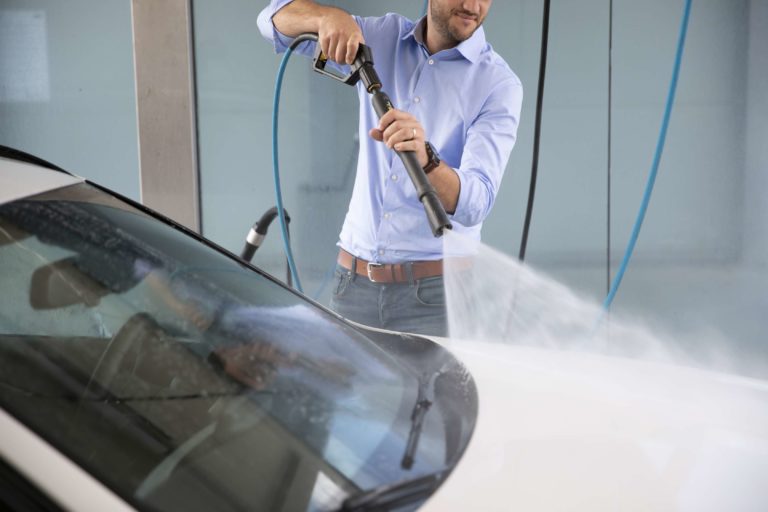 Man die zijn witte wagen wast in self carwash met een hoge druk reiniger.