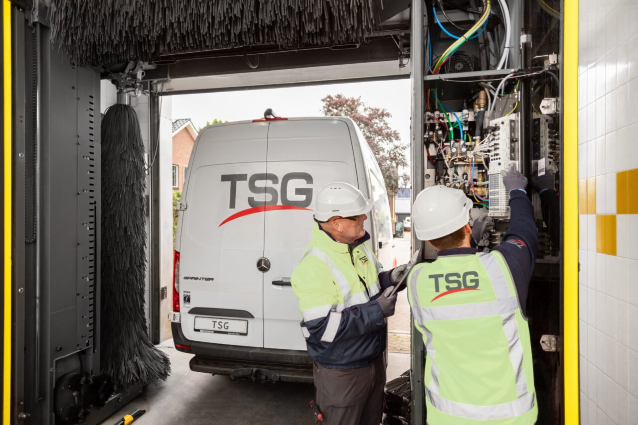 Twee techniekers installeren een roll-over. De machine is open om mechanische werken te kunnen uitvoeren.