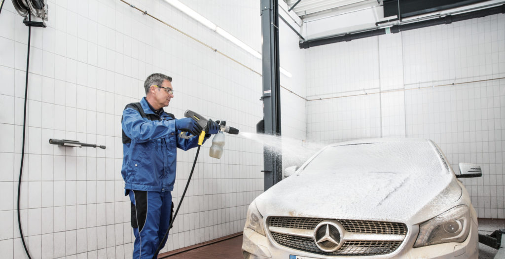 Un homme qui lave sa voiture blanche dans un selfwash.
