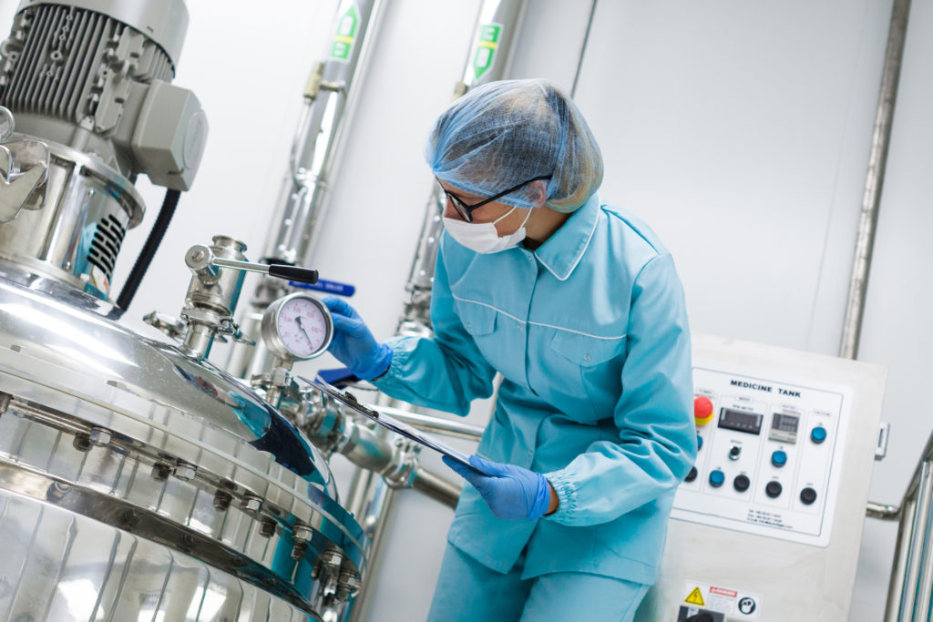 Wetenschapper in blauw labo-uniform die zich bukt over een compressor met een tablet in haar handen.