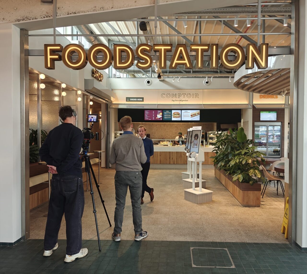 Klant geeft interview in het foodstation naast de order kiosk. Twee camera mensen nemen het interview op.